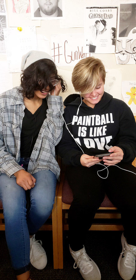Senior Ariel Aguilar puts in an earbud with junior Maycie Meaders to listen to their favorite 90s music. The two celebrated Homecoming week, Rock of the Ages with their classmates.