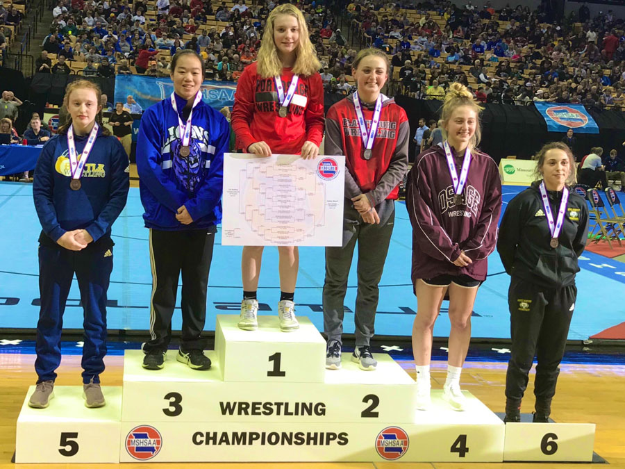 Freshman Haley Ward stands at the top of the podium with the 130 pound Championship bracket poster in her hands. Ward is the first Individual Girls Wrestling State Champion in FOHS history.