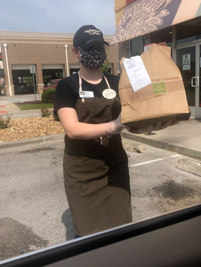 Working during the COVID-19 Shut Down, Junior Aubri Stewart hands a Panera Bread order to a curb-side customer. Food service companies like Panera were considered essential jobs which allowed teenage employees to still work during the Jackson County Stay at Home Order.