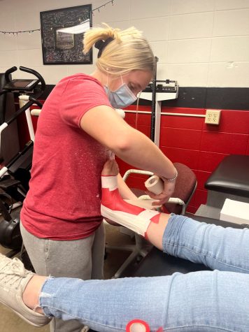 TAPE IT.  Securing the ankle, Freshman McKenna Gilpin applies athletic tape to a student  prior to practice. Students interested in athletic training or rehabilitation services can serve as assistants to the head athletic trainer at the school.