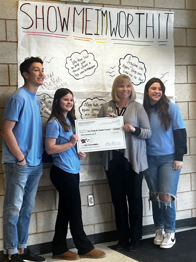 TEAMWORK. Missouri School Board Association Director for the Center of Education Safety Amy Roderick (Right Center) presents Senior Chase Stumfoll (Far Left), Junior Ava Flaig (Left Center) and Freshman Aubrey Miller (Far Right) with a check for their winning poster entry. Ms. Roderick hopes contests like the Bus Safty PSA gives students the opportunity to solve real world problems together. “We like to do this with students so its empowering for them to take control of their environment and promote safety,” Ms. Roderick said.