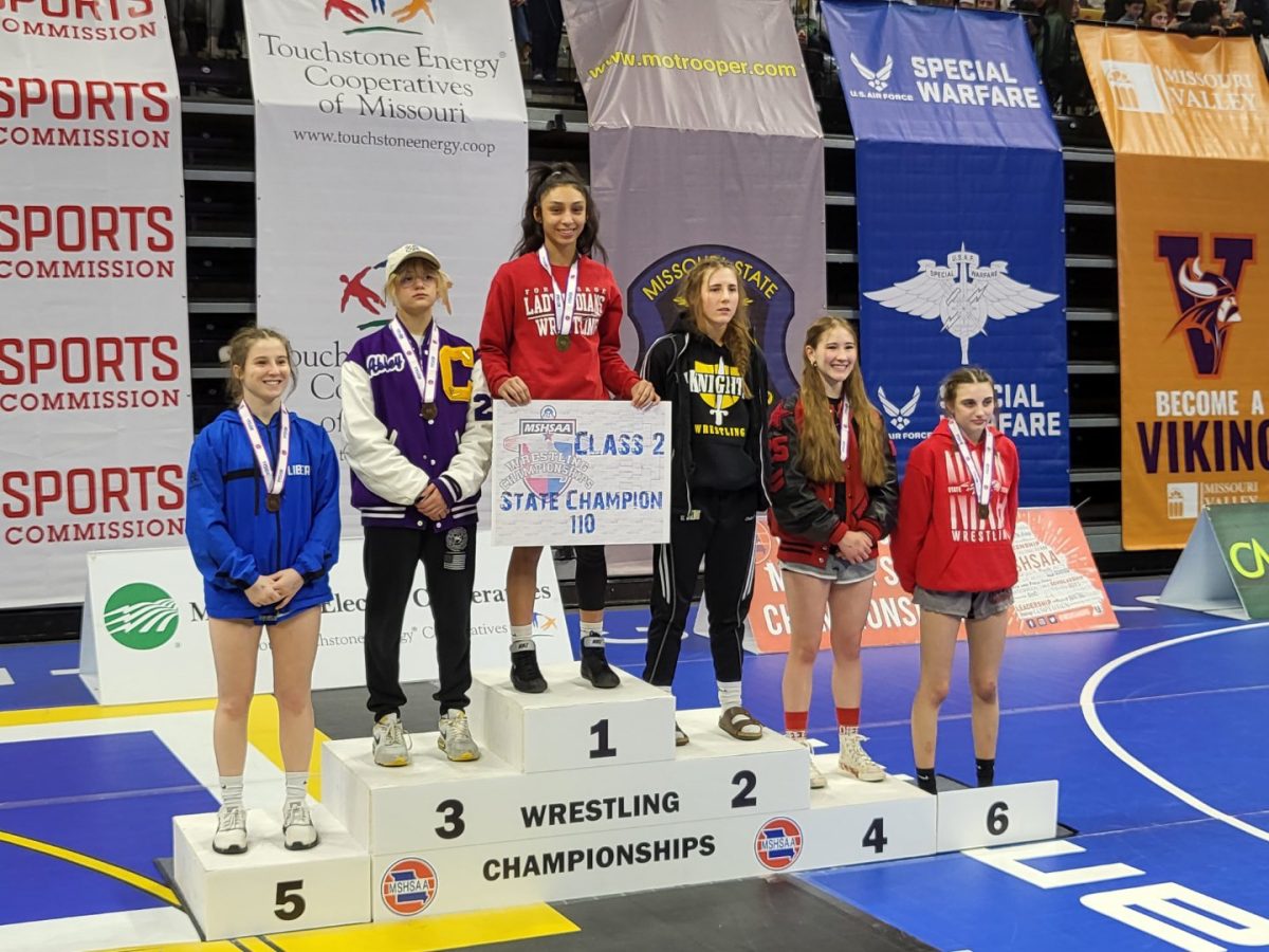 TOP+OF+THE+PODIUM.+Holding+the+title+card%2C+Senior+Aroma+Marrufo+stands+in+the+champions+spot+for+the+110+weight+class+at+the+MSHSAA+Girls+Class+2+2024+State+Wrestling+tournament.+Marrufo+is+the+second+girls+state+champion+in+school+history.++I+was+so+happy+and+felt+accomplished%2C++Marrufo+said.